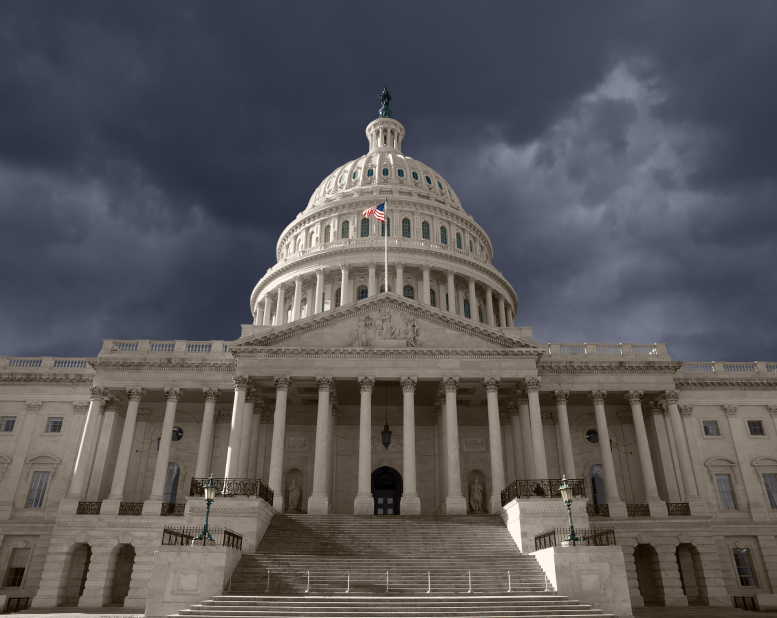 U.S. Capitol Building with white dome and American flag under dramatic dark storm clouds, viewed from front steps