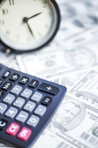 Black calculator and analog clock resting on a spread of US dollar bills, symbolizing financial time management.