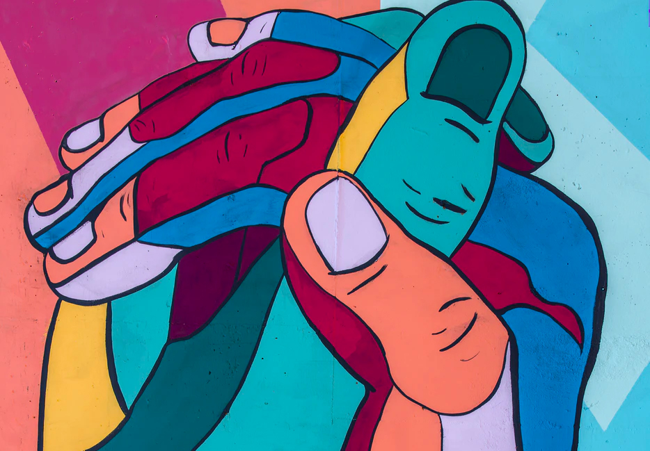 Colorful street mural depicting multiple interlocked hands in bold shades of teal, red, blue, orange, and pink on a vibran...