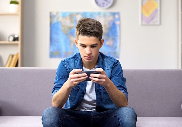 Gadget addicted Caucasian teenager playing game on smartphone, wasting time
